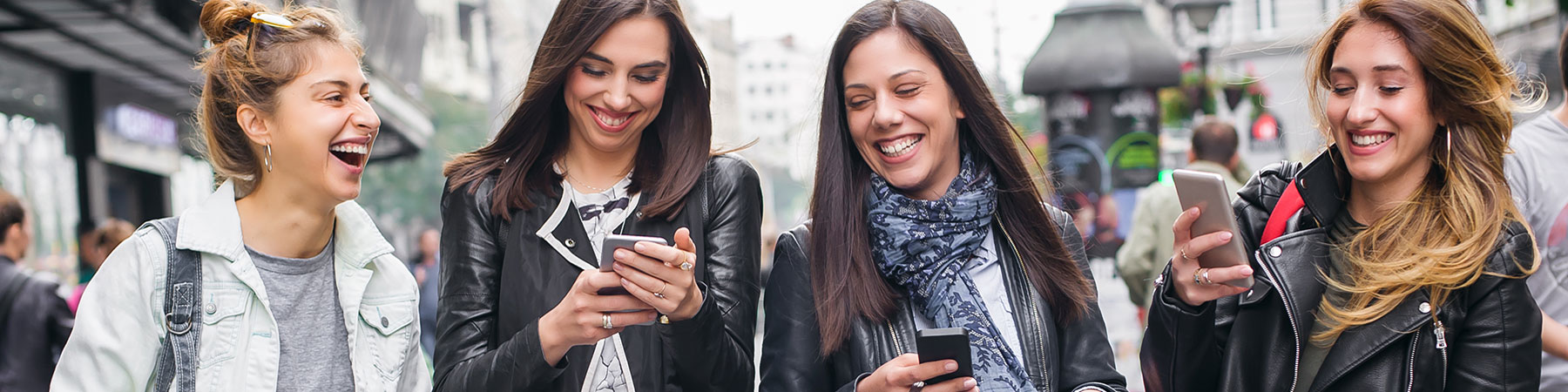 Four happy friends walking on the street and using cellphones