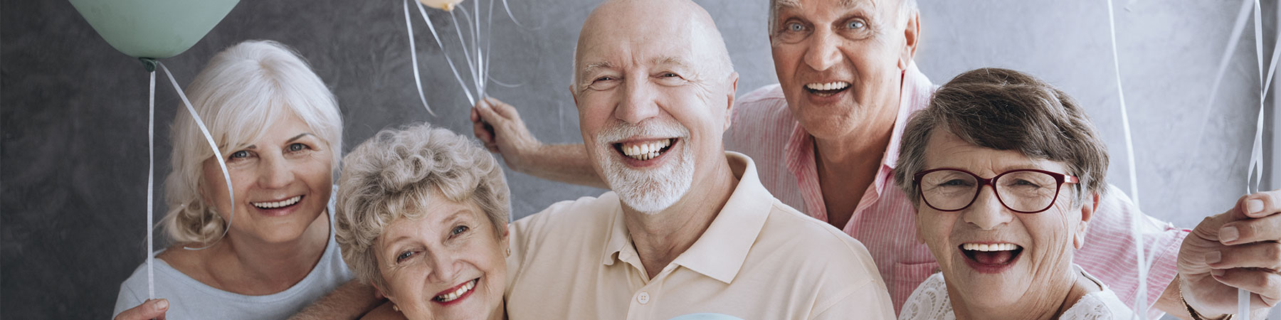 A group of happy, senior friends holding colorful balloons while posing at a party