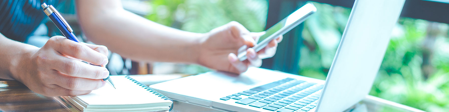 Business woman hand is writing on a notepad with a pen and using a mobile phone