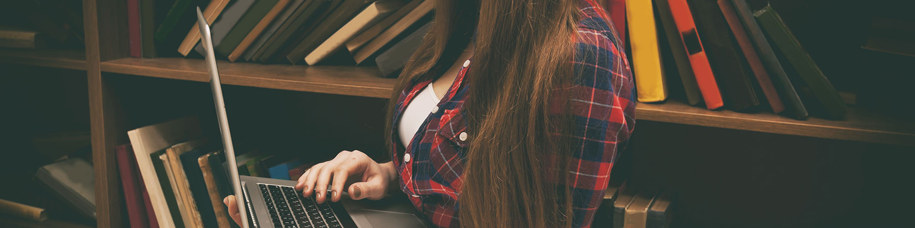 Young woman holds a laptop and book shelves on background